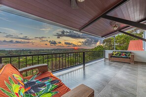 Un balcone con vista sul tramonto, un divano in vimini e un pavimento piastrellato.