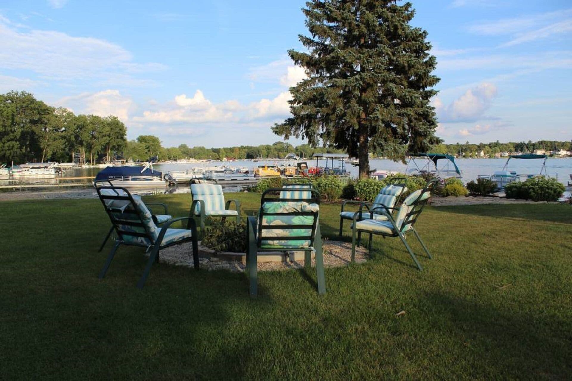 Un espace extérieur verdoyant avec une table et des chaises, un grand arbre et une vue sur des bateaux sur un lac.