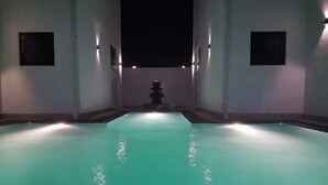 A swimming pool with a central fountain, surrounded by walls with small windows.