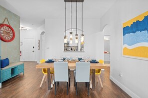 A dining area with a wooden table set for four, light blue chairs, and a hanging light fixture above. - Mickey Mouse Condo. Kid friendly Condo in Windsor Hills Resort.2 miles to Disney (Kissimmee)