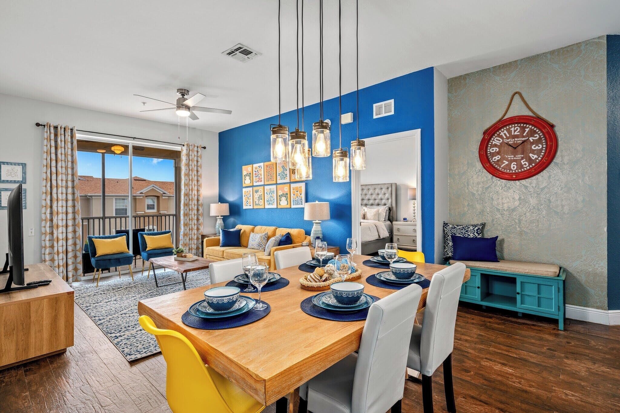 A dining area with a wooden table set for four, a sofa, and a clock on the wall.