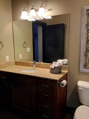 Une salle de bain avec un lavabo doté d’un plan de travail en granit, un miroir, un distributeur de serviettes et des toilettes.