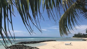 A beach with clear turquoise water, a sandy shore, and a few rocks.