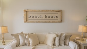 A bedroom with a bed, two bedside tables, and a wall-mounted sign that reads "beach house".