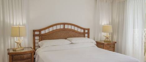 Una cama bien tendida con cabecera de madera, dos mesitas de noche con lámparas y cortinas blancas.