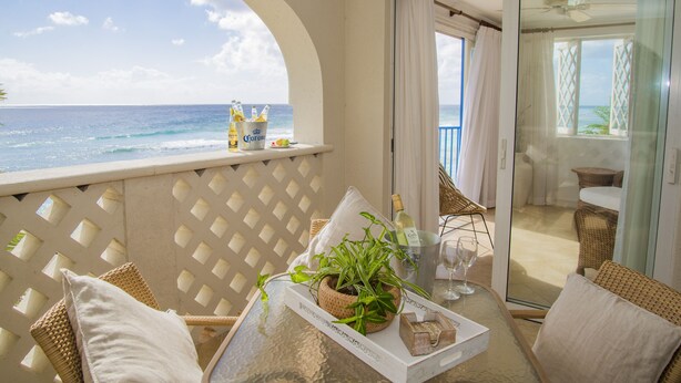 A balcony with wicker furniture, a glass table, and a view of the ocean.