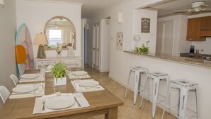A dining area with a wooden table set for six, a kitchen with a granite countertop, and a mirror reflecting the room.