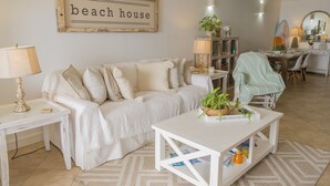 A cozy living room with a white sofa, a coffee table, and a framed sign that reads "beach house".