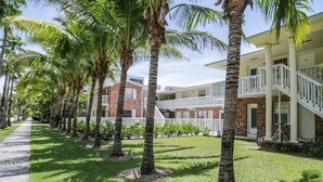 A row of palm trees lining a pathway leading to a building with a brick facade and white balconies. - SEASONAL RENTAL IN KEY BISCAYNE (Key Biscayne)