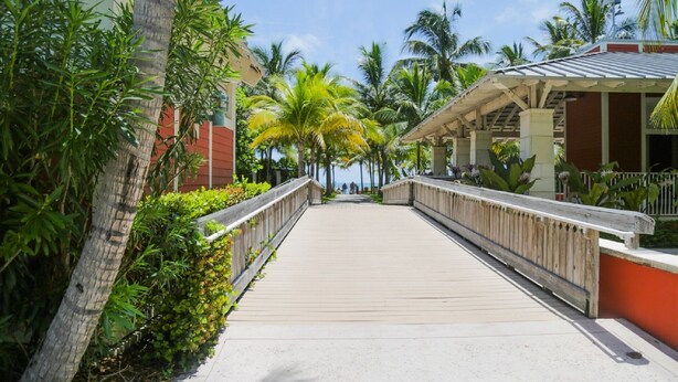 A wooden boardwalk leading to a building with a red facade and a covered area with a metal roof. - SEASONAL RENTAL IN KEY BISCAYNE (Key Biscayne)
