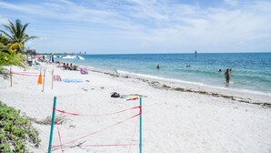 A beach with a volleyball net, umbrellas, and people swimming. - SEASONAL RENTAL IN KEY BISCAYNE (Key Biscayne)