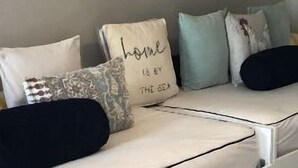 A white sofa with multiple cushions, a mirror above it, and a small wooden chair. - SEASONAL RENTAL IN KEY BISCAYNE (Key Biscayne)