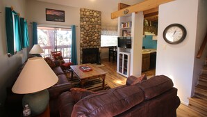 A living room with a brown leather sofa, a wooden coffee table, and a stone wall. - Only steps to the slopes!!! (Angel Fire)