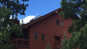 A multi-story building with a red exterior, balconies, and a stone retaining wall. - Only steps to the slopes!!! (Angel Fire)