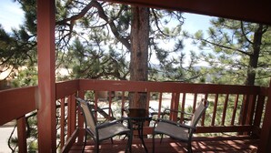 A wooden deck with two chairs and a small table, surrounded by pine trees. - Only steps to the slopes!!! (Angel Fire)