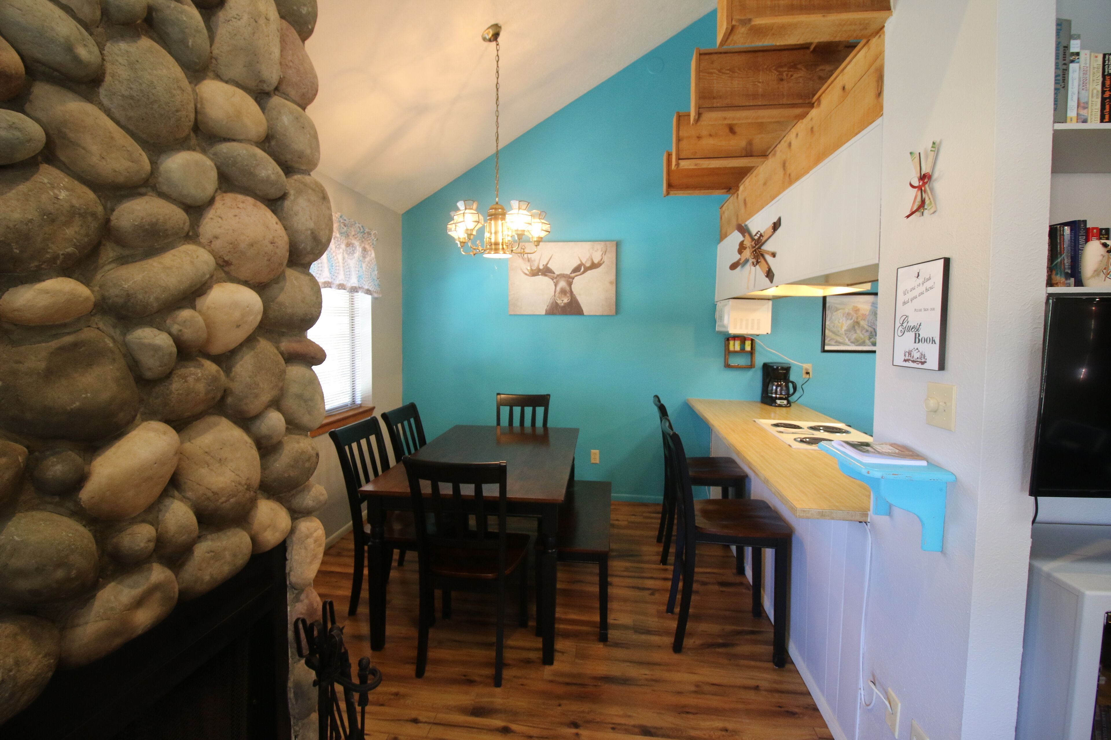 A dining area with a stone wall, wooden table, chairs, and a chandelier.