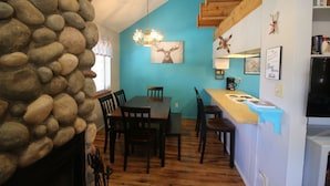 A dining area with a stone wall, wooden table, chairs, and a chandelier. - Only steps to the slopes!!! (Angel Fire)