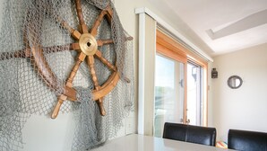 Un'area pranzo con un tavolo grande e due sedie nere, una ruota di timone in legno e una decorazione murale a rete.