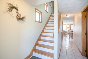 Un escalier avec des marches en bois menant à un palier, une guirlande décorative accrochée au mur, et un couloir avec un sol carrelé et des portes en bois.