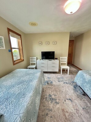 Une chambre avec deux lits, une télévision, une commode et une fenêtre.