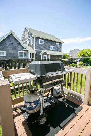 Un barbecue sur une terrasse en bois, avec une bouteille de propane marquée « Blue Rhino » et un chariot pour barbecue.