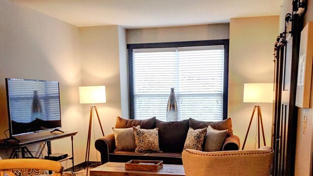 A living room with a sofa, armchair, coffee table, TV, and lamps.