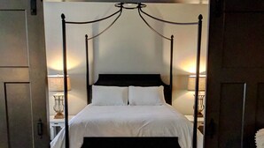 A four-poster bed with white linens, a wooden floor, and two bedside lamps.