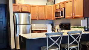 A kitchen with wooden cabinets, stainless steel appliances, and a bar area with stools.
