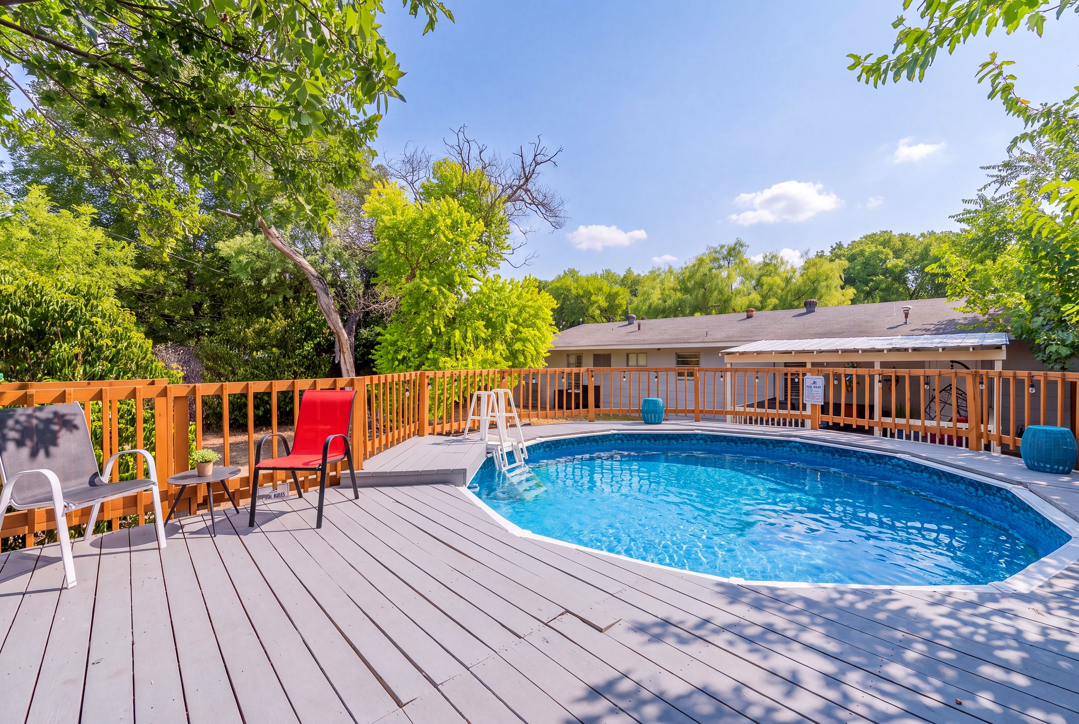 Una piscina con cubierta de madera, una silla roja y una mesa blanca.