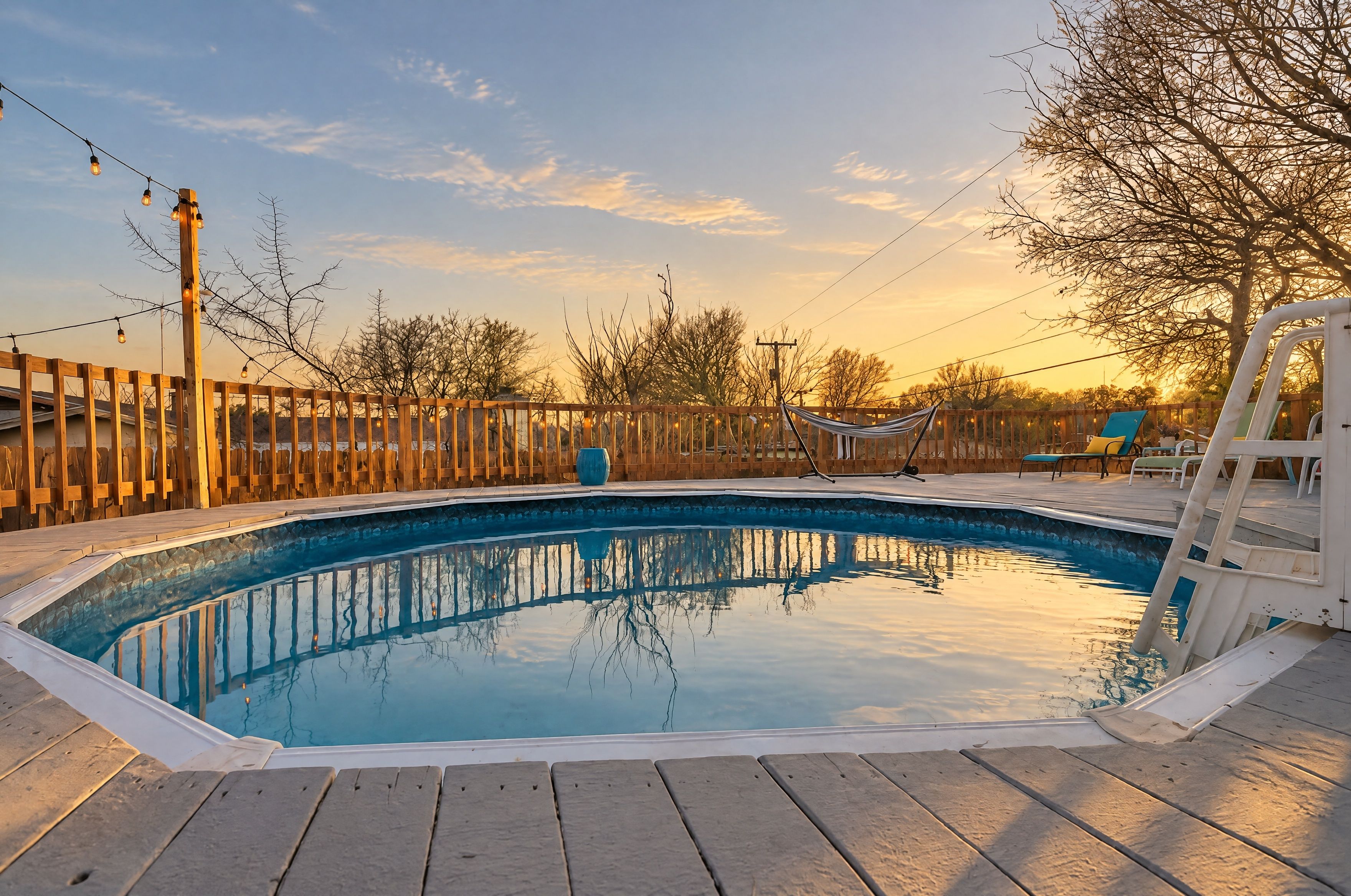 Una piscina con bordo in legno, circondata da una recinzione in legno e alberi.