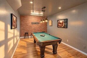 A pool table in a room with a brick wall, wooden flooring, and ceiling lights. - Private Pool, Gameroom, Fire pit & BBQ near the Medical center (San Antonio)