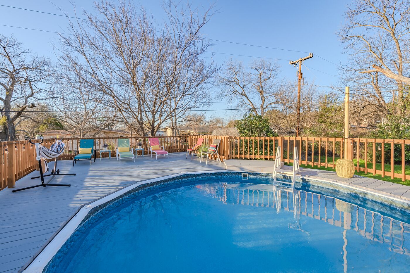 Piscina con bordo in legno, circondata da una recinzione di legno e alberi.