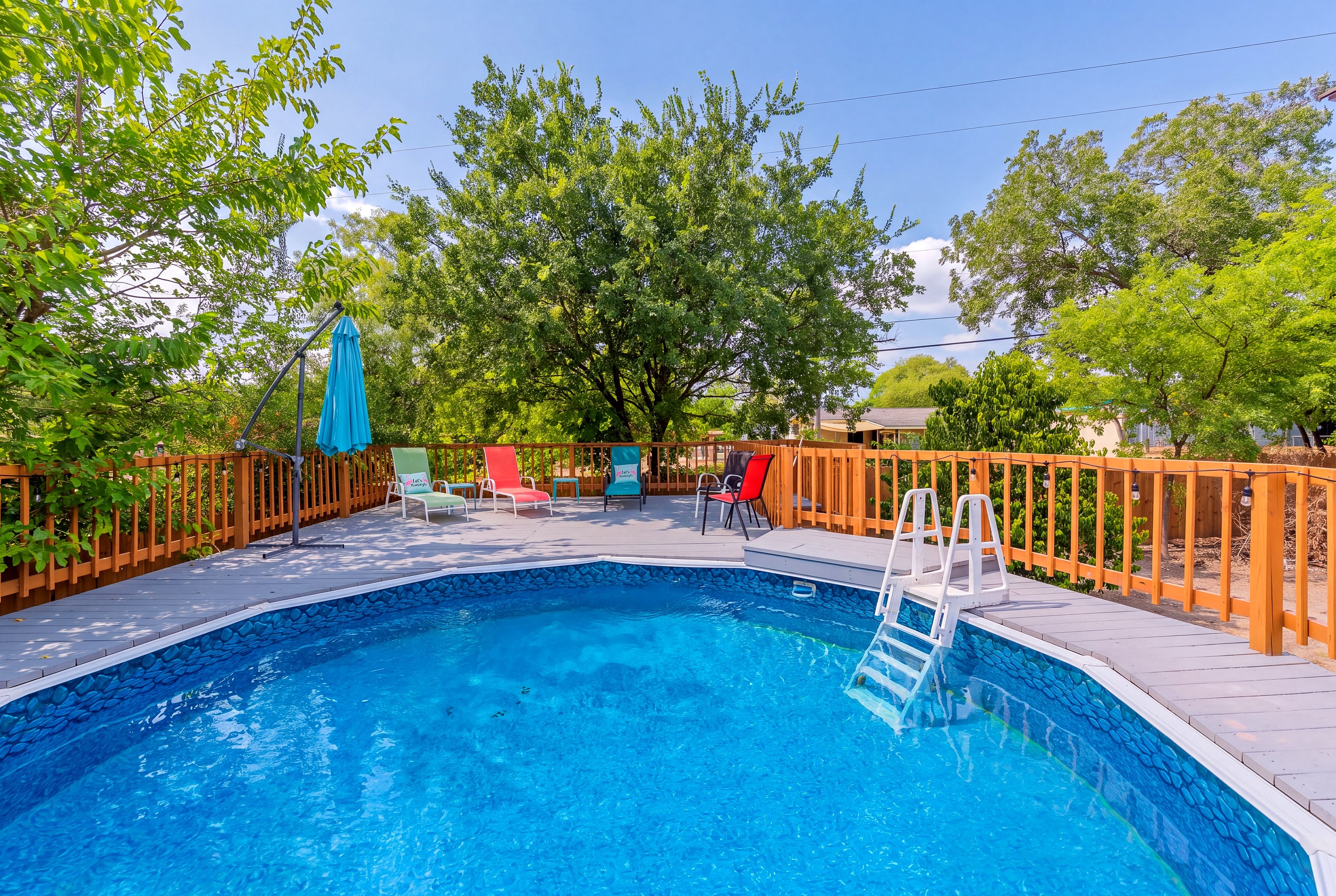 A swimming pool with a stone-lined edge, surrounded by a wooden deck and a wooden fence.