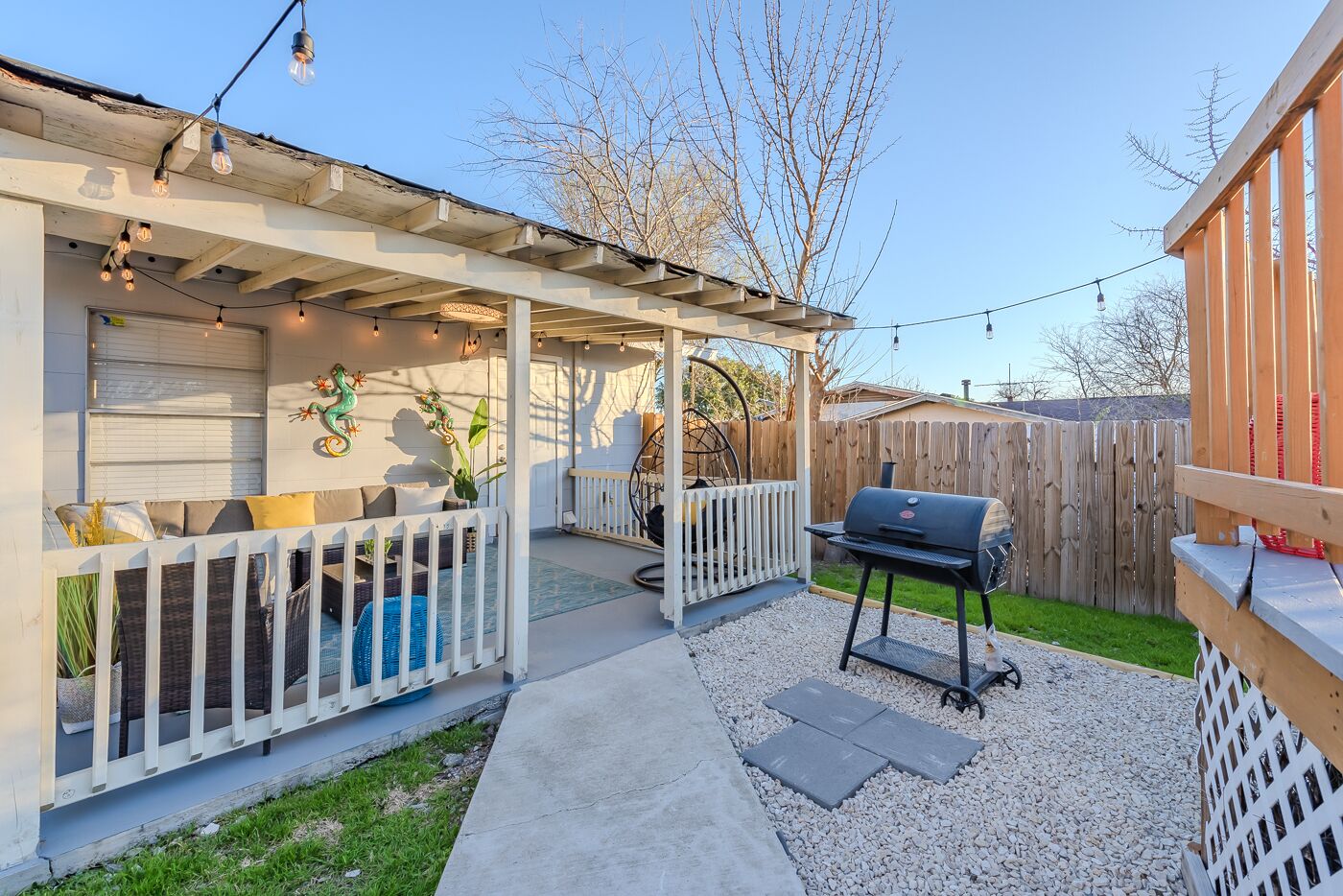 Un patio cubierto con mobiliario exterior, una parrilla de barbacoa y luces colgantes.