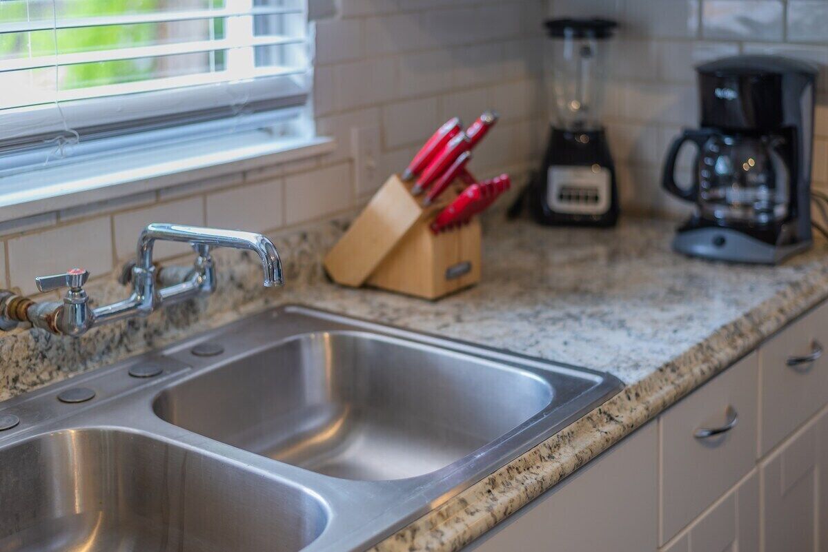 Una cocina con un lavamanos doble de acero inoxidable, una cafetera y una licuadora sobre la encimera.