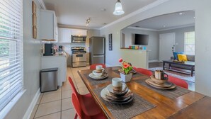 Una cocina moderna con armarios blancos, un microondas y un refrigerador. Hay una zona de comedor con una mesa de madera y sillas rojas.