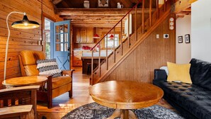 L’intérieur d’un chalet accueillant, avec un escalier en bois, un coin repas, un canapé et une cuisine en arrière-plan.