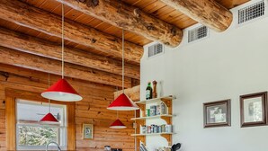 Une cuisine avec un plafond en bois, un grand îlot central doté de tabourets et des suspensions rouges.