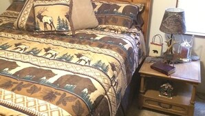Een bed met een geborduurde deken, een houten hoofdbord, een nachtkastje met een lamp en een bord met een welkomstboodschap.