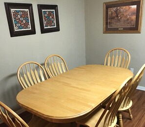 Comedor con mesa de madera y seis sillas. Hay dos cuadros en la pared.