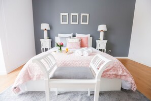 Quarto bem arrumado com cama, duas mesas de cabeceira, uma cadeira e uma prateleira na parede.