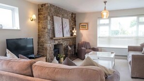 A living room with a stone fireplace, a television, and a large window with blinds.