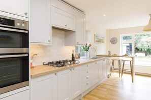 Une cuisine moderne avec des meubles blancs, un four encastré, une cuisinière à gaz et un coin repas comprenant une table et des chaises.