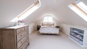 A bedroom with a sloped ceiling, a bed, a dresser, bedside tables, and a built-in shelving unit.