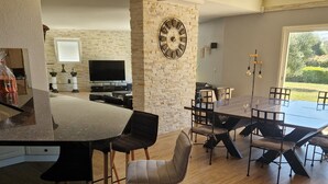 Une cuisine moderne avec un mur d’accent en pierre, une grande horloge et un coin repas offrant une vue sur le jardin.