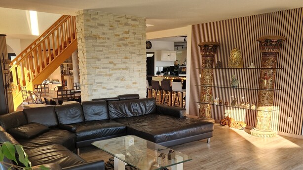 Un salon moderne avec un canapé d’angle, une table basse en verre et un mur décoratif en pierre.