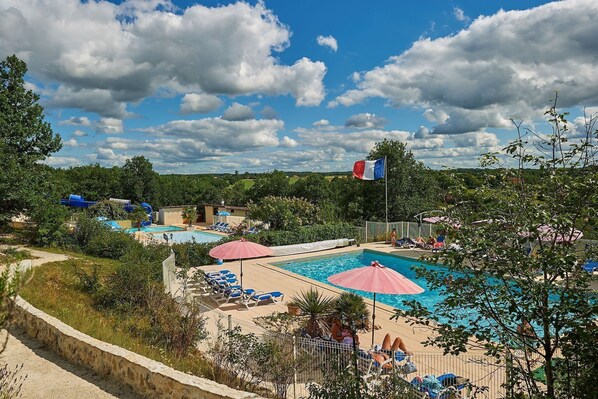 Un espace piscine comprenant plusieurs bassins, des chaises longues, des parasols et un drapeau.