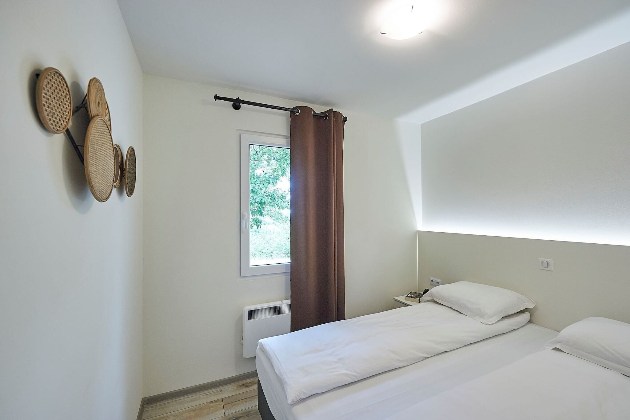 Ein Schlafzimmer mit einem Bett, einem Fenster mit Blick auf Grünflächen, einem an der Wand befestigten Regal mit Körben und einer Gardinenstange.