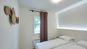 Ein Schlafzimmer mit einem Bett, einem Fenster mit Blick auf Grünflächen, einem an der Wand befestigten Regal mit Körben und einer Gardinenstange.