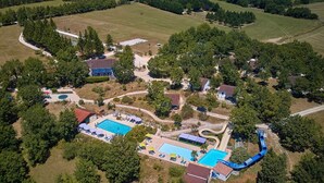 Eine Vogelperspektive eines Resorts mit mehreren Schwimmbecken, einer Wasserrutsche und umliegenden Waldgebieten.